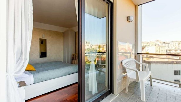A balcony with a bed, a chair, and a view of buildings. - The House of the Pine Nativity (Napoli)
