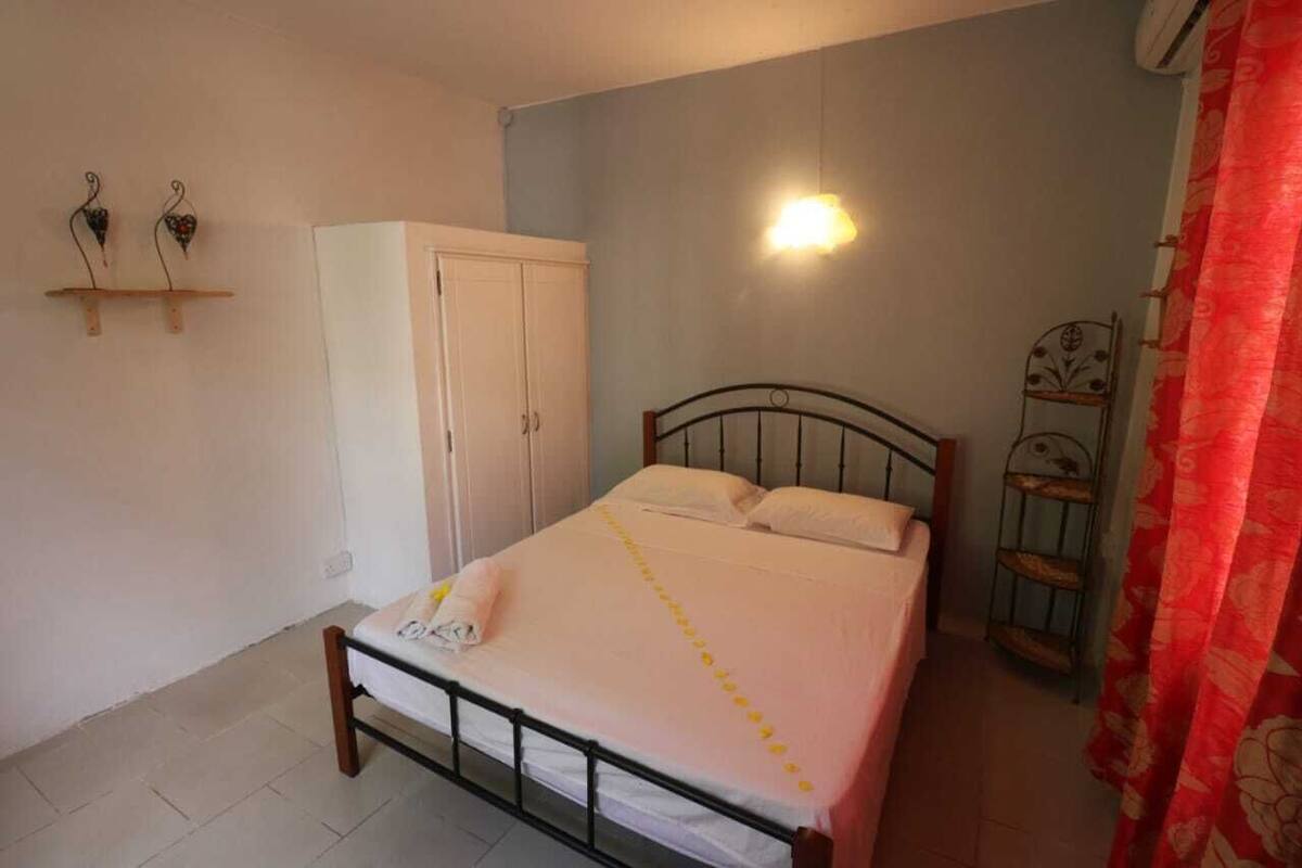 A bedroom with a bed, a wardrobe, a wall-mounted light, and a metal shelf.