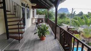 A balcony with a wooden staircase, a potted plant, and a view of a mountain and greenery. - Isola Bella Luxury Villa (La Gaulette)