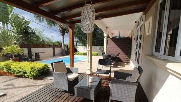 A covered outdoor area with wicker furniture, a glass table, and a hanging light fixture. - Isola Bella Luxury Villa (La Gaulette)