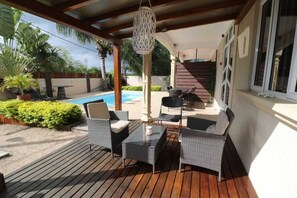 A covered outdoor area with wicker furniture, a glass table, and a hanging light fixture.