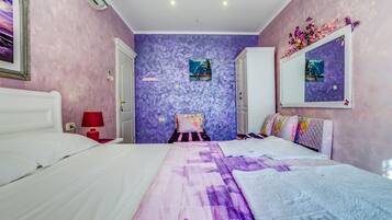 A bedroom with a bed, a nightstand, a red lamp, a mirror, and a door.