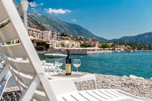 A beachside view with a chair, a bottle of wine, and two glasses on a table. - Villa Donkovic (Kotor)