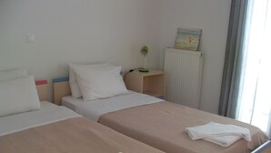 Ett hotellrum med två sängar, ett element, ett litet bord med en lampa och ett fönster med gardiner.