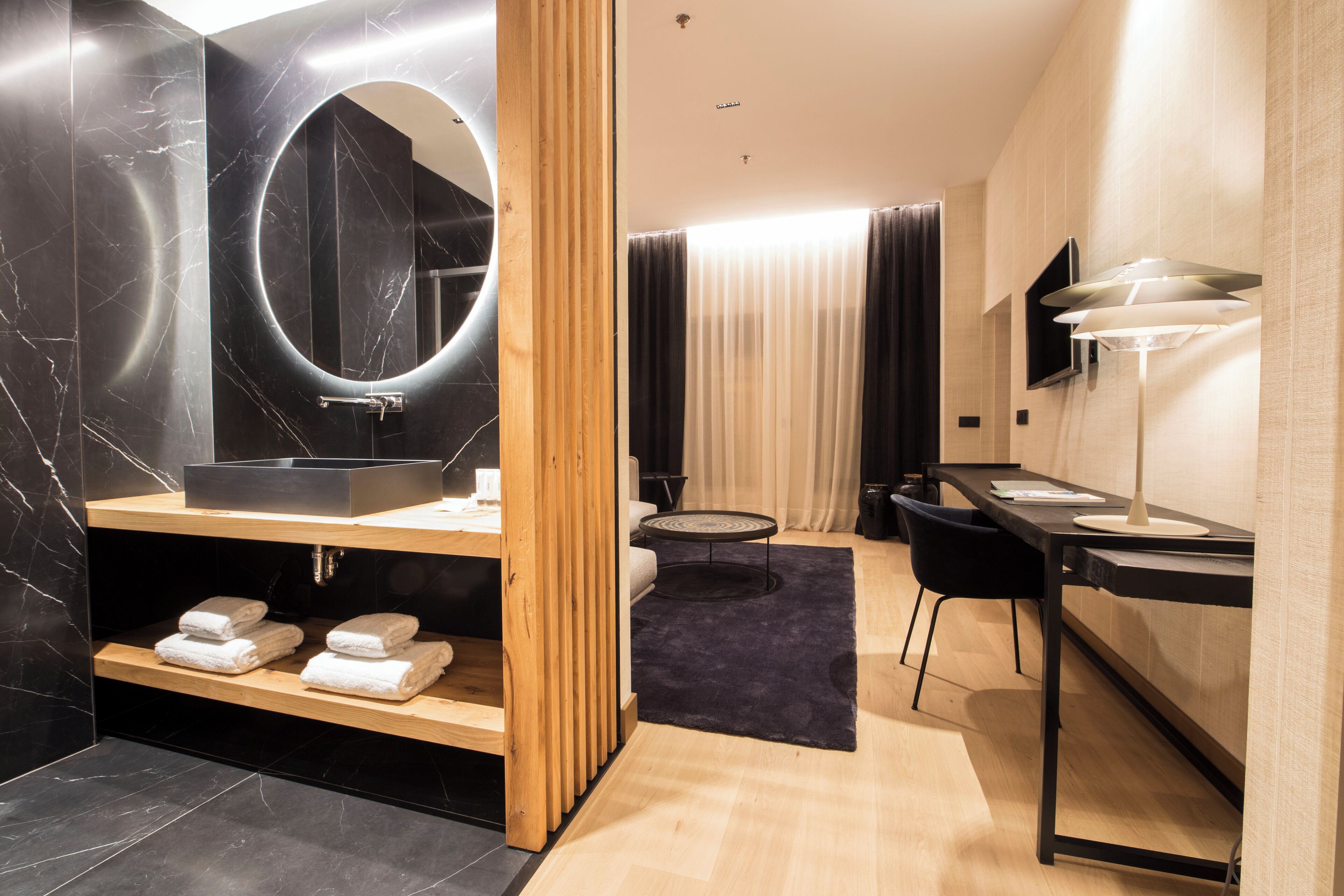 Een moderne badkamer met een grote spiegel, een houten wastafelmeubel en een zwart wastafelbakje.