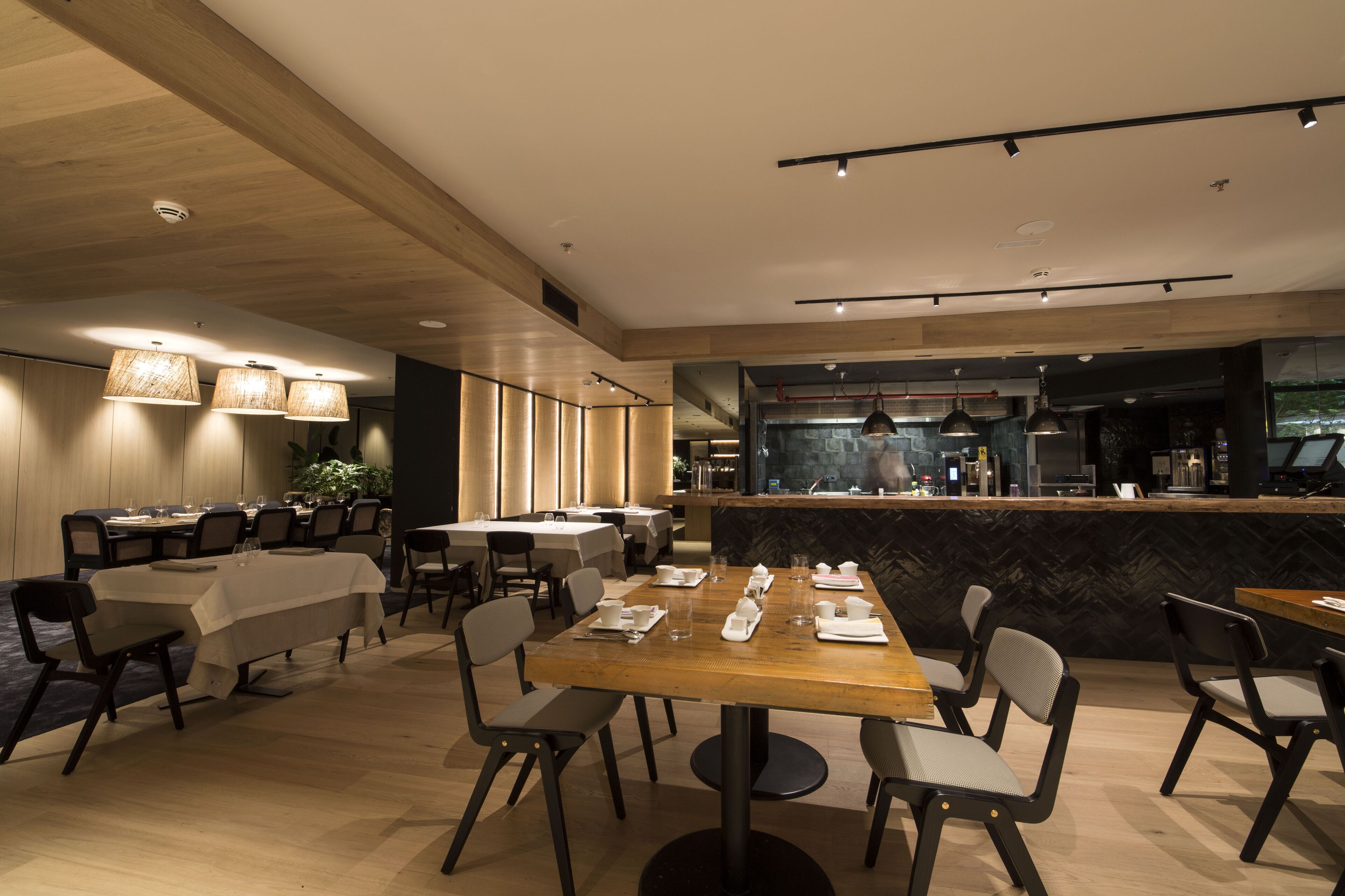 Un espace de restauration moderne avec des tables dressées pour le service, un bar et une vue sur la cuisine.