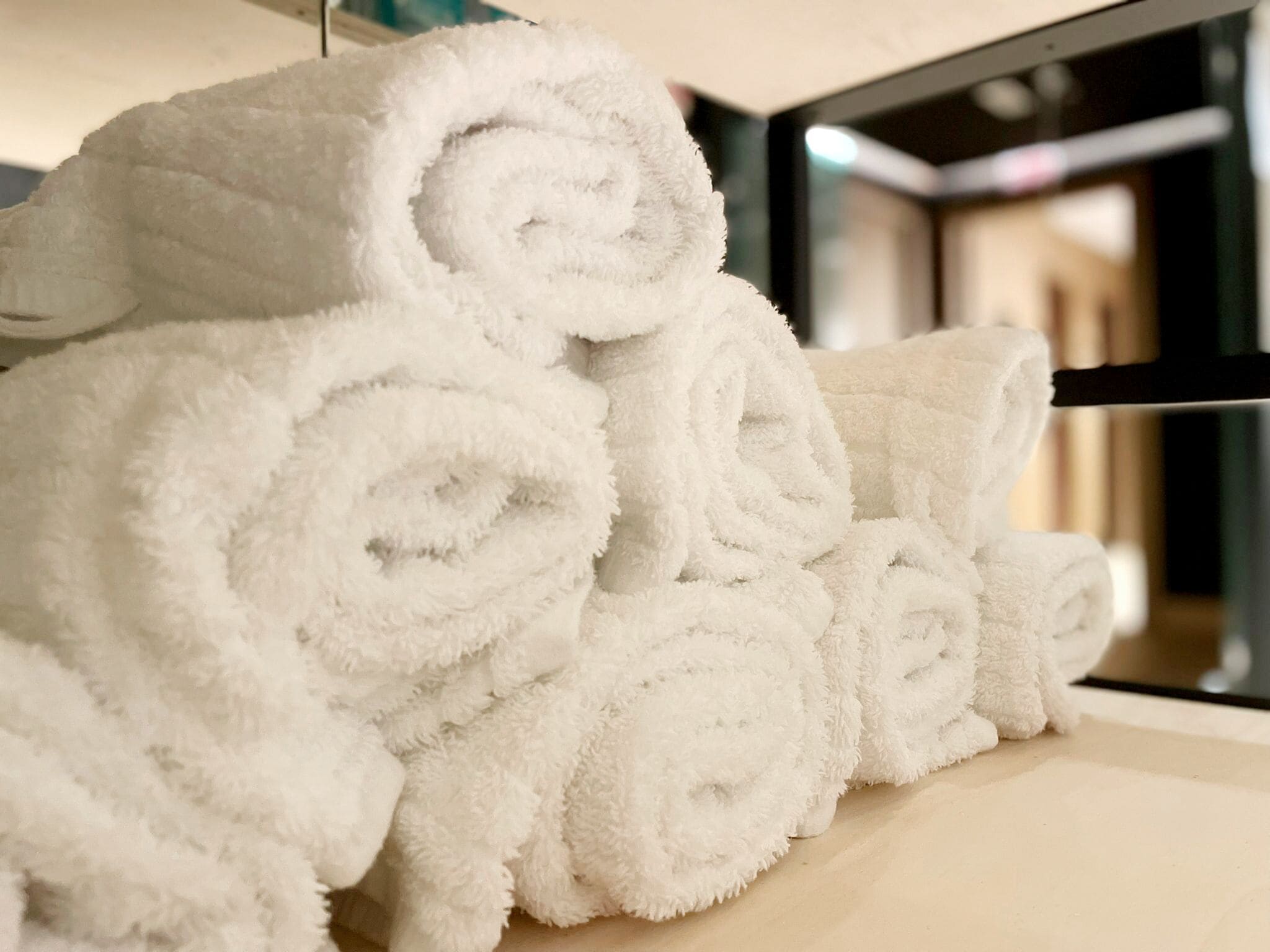 Una pila de toallas blancas enrolladas ordenadamente sobre una superficie de madera en una habitación de hotel.