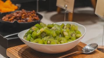 A bowl of sliced kiwi fruit on a wooden board with a spoon beside it.