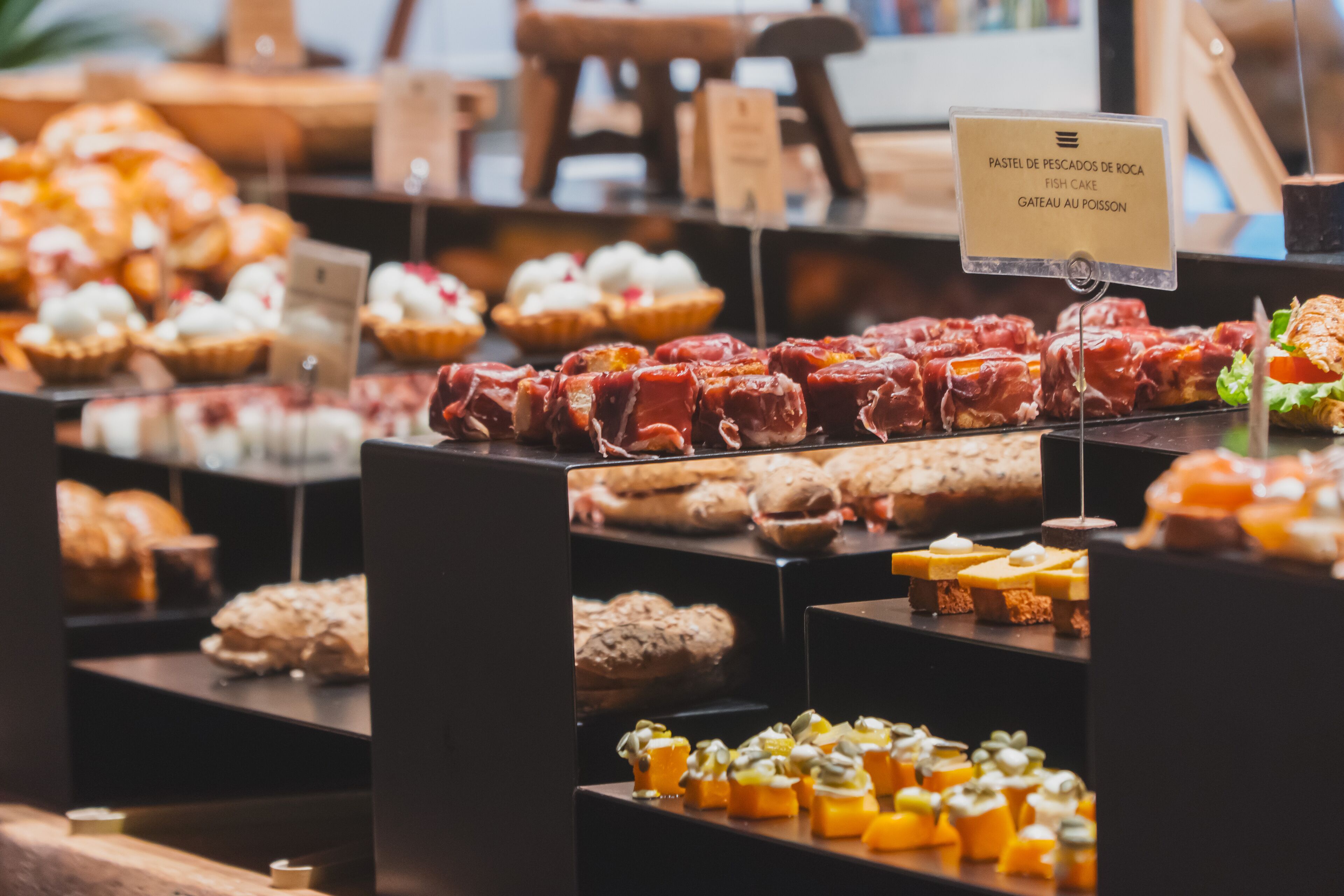 Variedad de alimentos exhibidos en un mostrador, entre ellos, pasteles, sándwiches y pequeños postres.