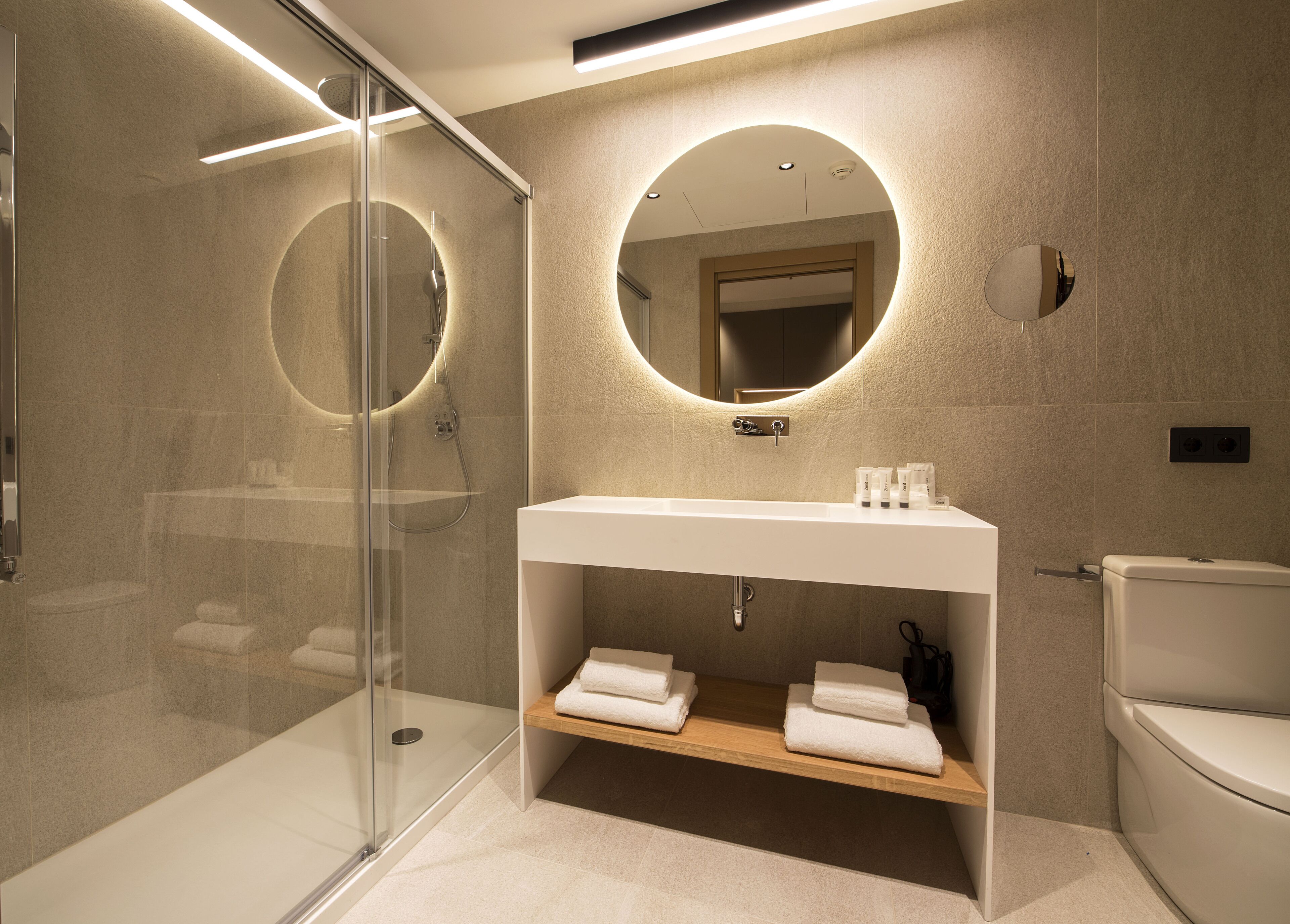 A modern bathroom with a glass-enclosed shower, a white sink with a mirror above, and a toilet.