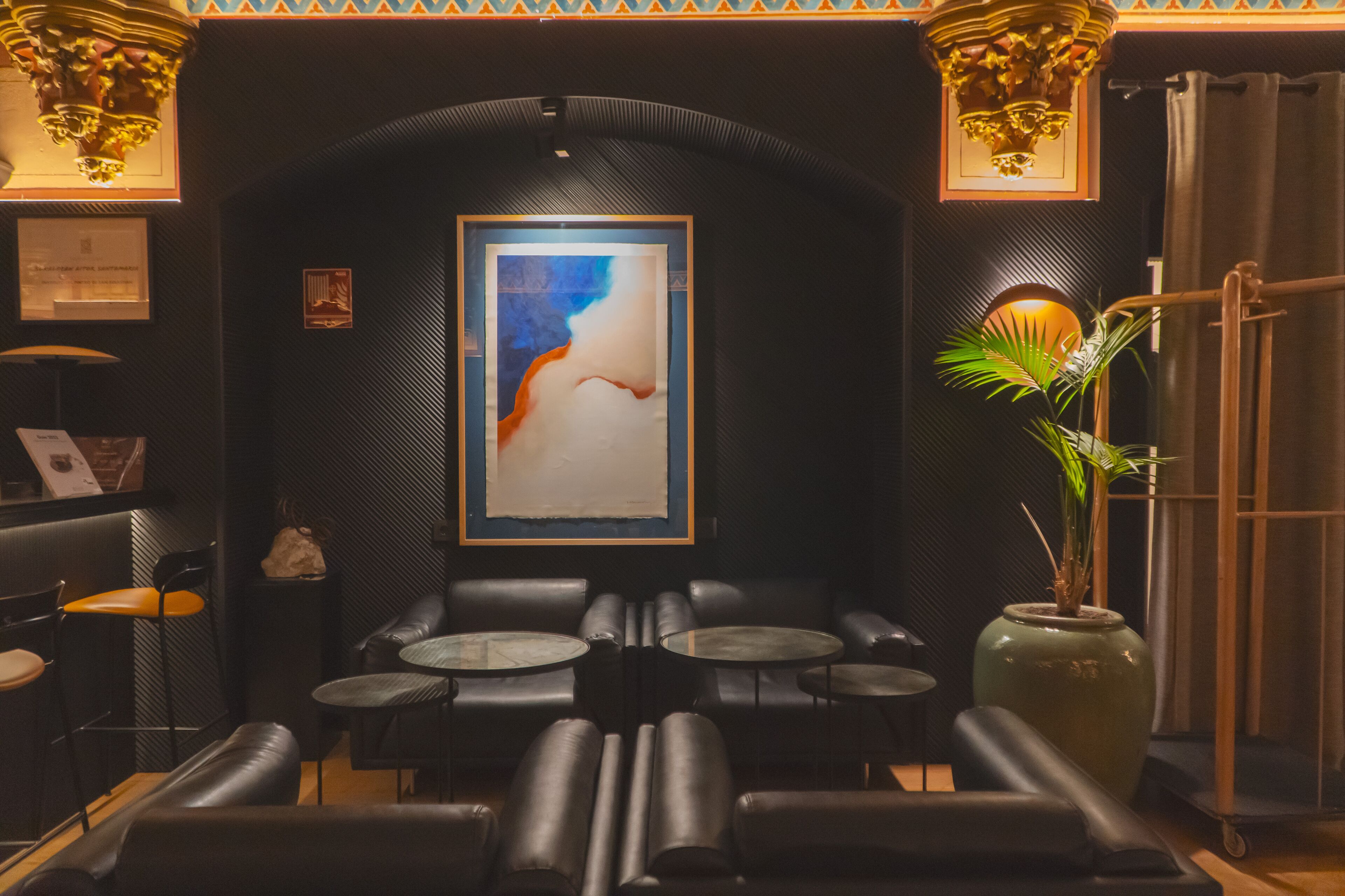 A dimly lit lounge area with leather seating, a large abstract painting on the wall, and a potted plant.