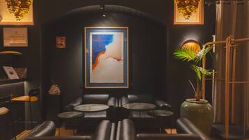 A dimly lit lounge area with leather seating, a large abstract painting on the wall, and a potted plant.