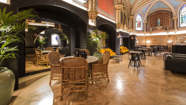 A spacious restaurant with high ceilings, ornate arches, and a variety of seating arrangements including wicker chairs and tables. - Hotel Zenit Convento San Martín (San Sebastián)