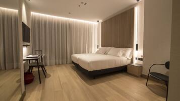 Una habitación de hotel moderna con cama, mesita de noche, silla y escritorio con otra silla.