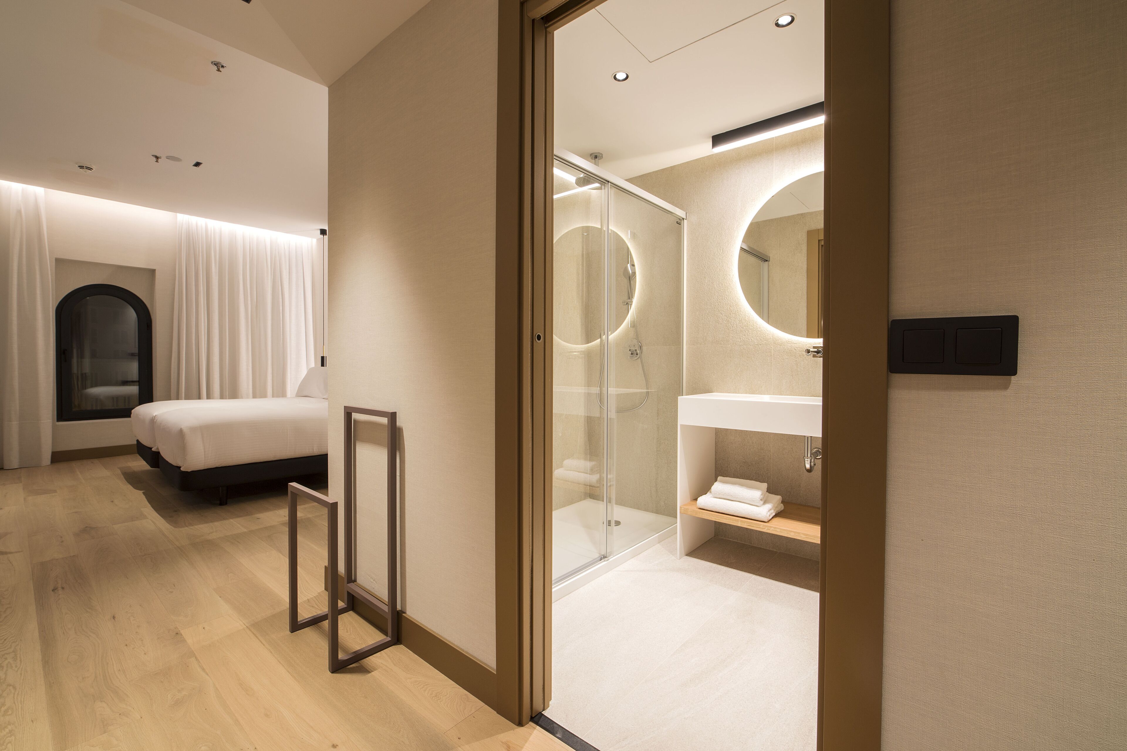 Une chambre d’hôtel moderne équipée d’un lit, d’une douche en verre et d’une coiffeuse avec un miroir.