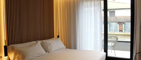 A hotel room with a large bed, a view of the outside balcony, and a modern design with wooden paneling on the wall.