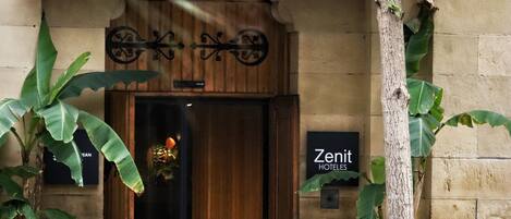 The entrance of the Zenit Hotels with a wooden door, a signboard, and potted plants.