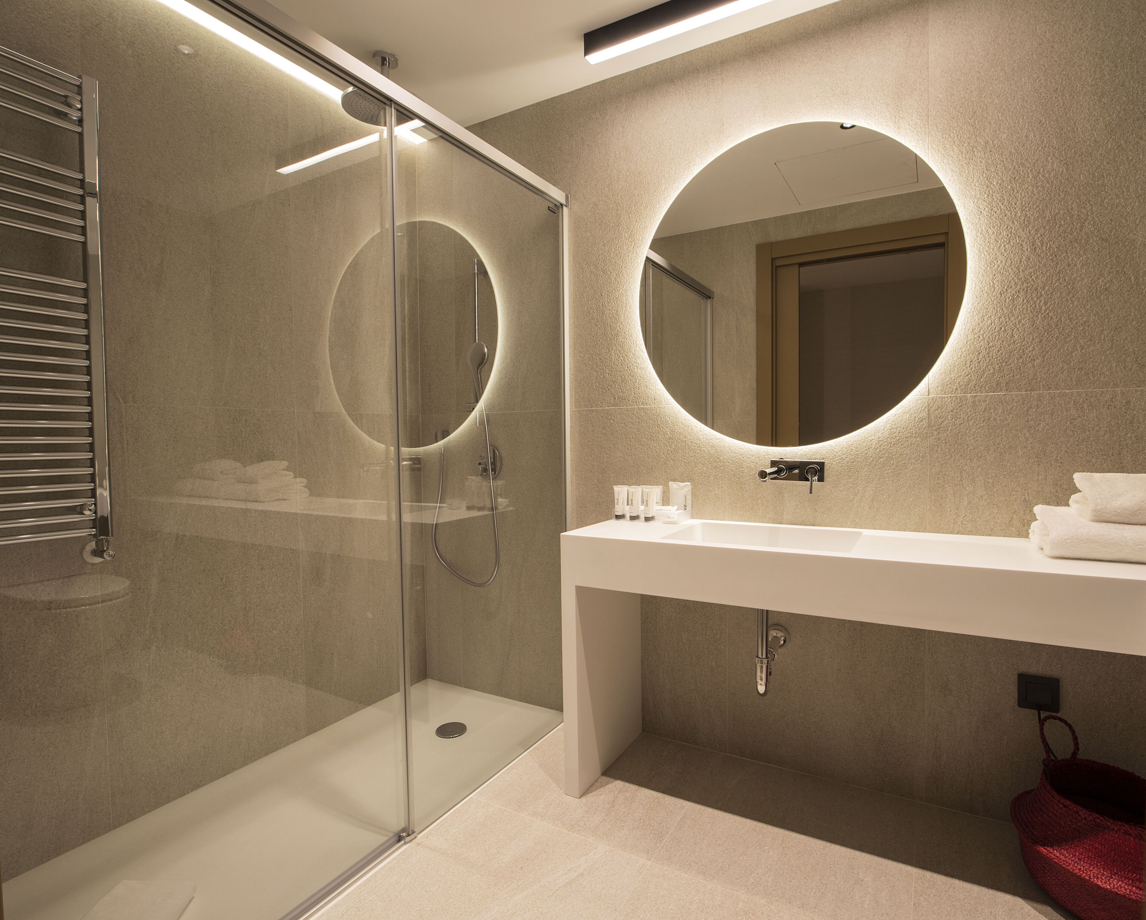 A modern bathroom with a glass-enclosed shower, a round mirror, and a white sink.