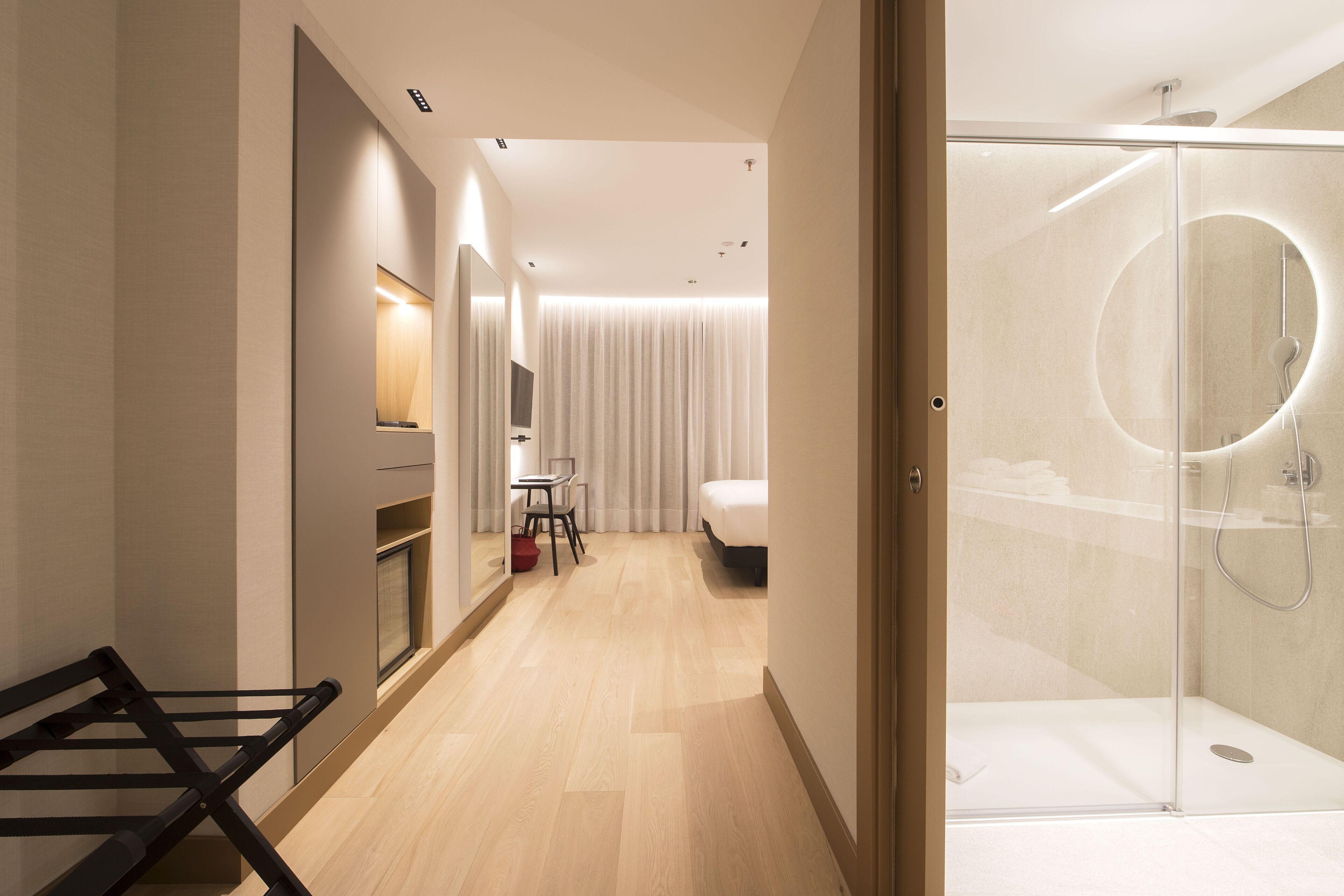 Une chambre d’hôtel moderne avec un plancher en bois, un lit, un bureau et un espace douche.