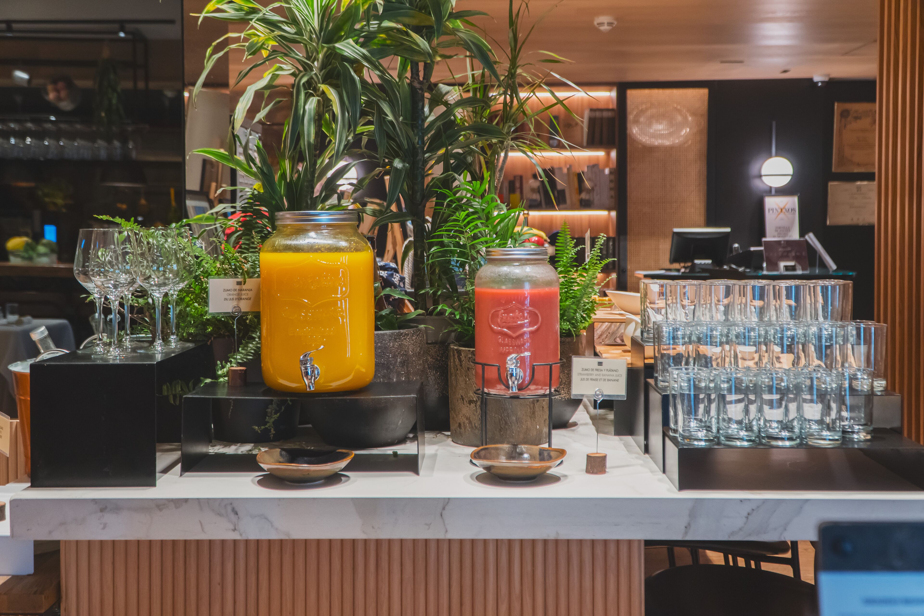 A bar area with a variety of drinks, including a large orange juice and a red smoothie, and a display of stacked glasses.