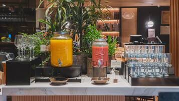 A bar area with a variety of drinks, including a large orange juice and a red smoothie, and a display of stacked glasses.