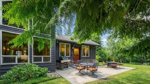 A modern house with a patio area featuring a grill, outdoor seating, and a well-maintained lawn.