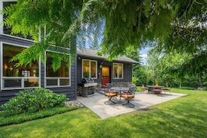 A modern house with a patio area featuring a grill, outdoor seating, and a well-maintained lawn.