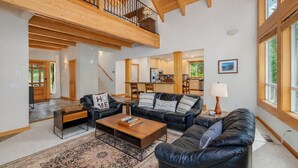 A spacious living area with a high ceiling, a balcony, and a view of the kitchen.