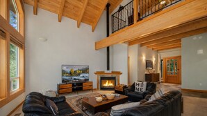 A spacious living room with a fireplace, leather sofas, a large TV, and a wooden ceiling.