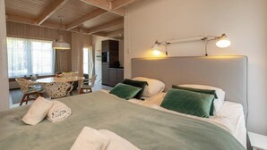A bedroom with a bed, bedside lamps, a dining area with a table and chairs, and a kitchen in the background. - Studio- Molenweg 27 | Zoutelande (Zoutelande)