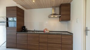 A modern kitchen with wooden cabinets, a stainless steel sink, and a built-in oven. - Studio- Molenweg 27 | Zoutelande (Zoutelande)