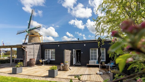 A modern house with a windmill, wooden deck, and outdoor seating area. - Studio- Molenweg 27 | Zoutelande (Zoutelande)