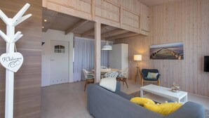 A cozy living room with a grey sofa, a wooden ceiling, and a painting of a pier. - Studio- Molenweg 27 | Zoutelande (Zoutelande)