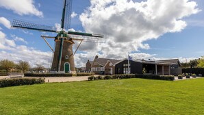 A traditional windmill with a green door, a modern building with a dark facade, and a well-maintained lawn in front. - Studio- Molenweg 27 | Zoutelande (Zoutelande)