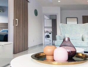 A modern living room with a round glass coffee table, a sofa, and a kitchen area in the background.