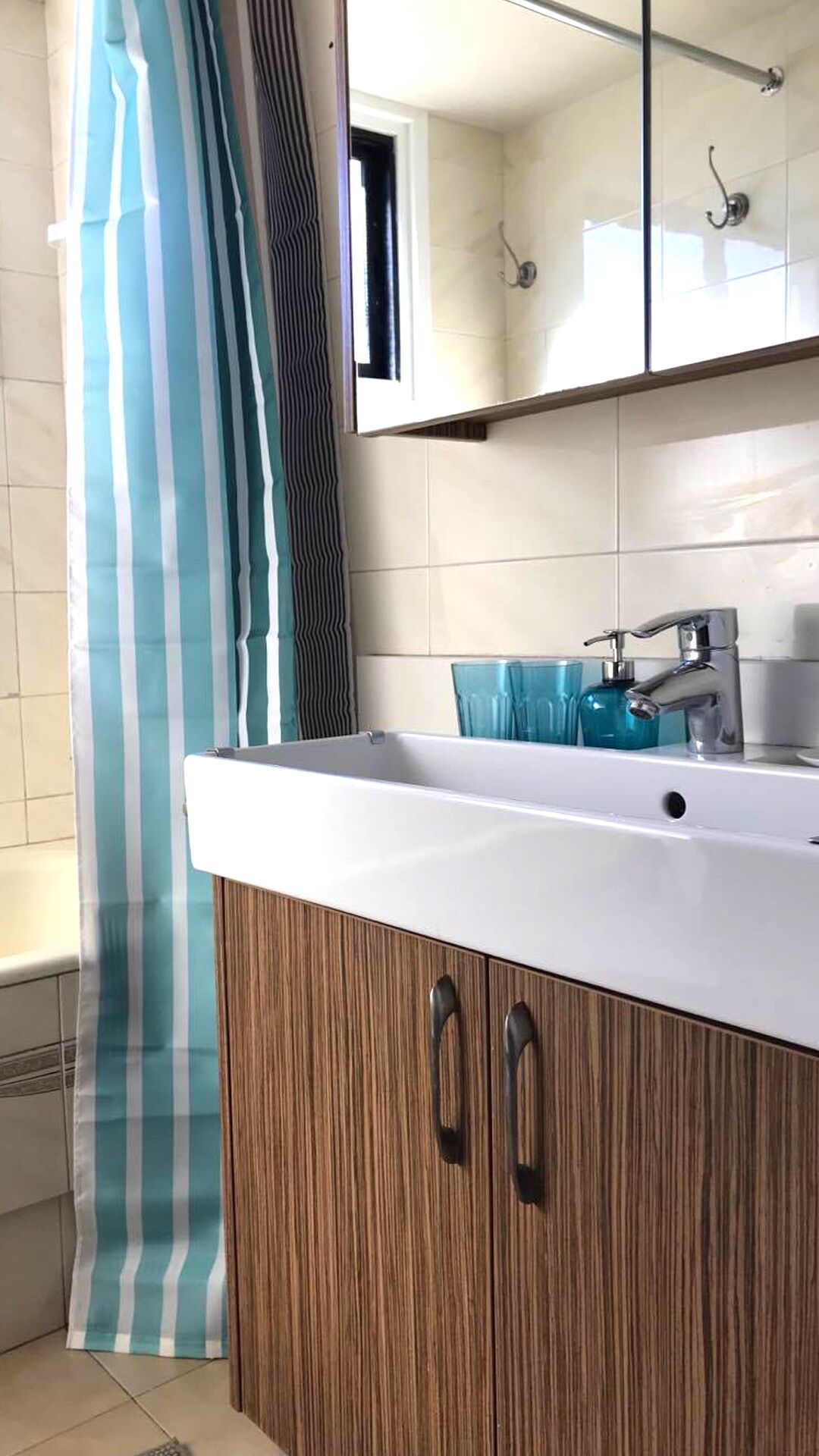 A bathroom with a white sink, wooden cabinets, a striped shower curtain, and a mirror above the sink.