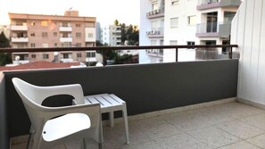 Un balcón con una silla de plástico blanco y una mesita pequeña, con vistas a una hilera de edificios residenciales.