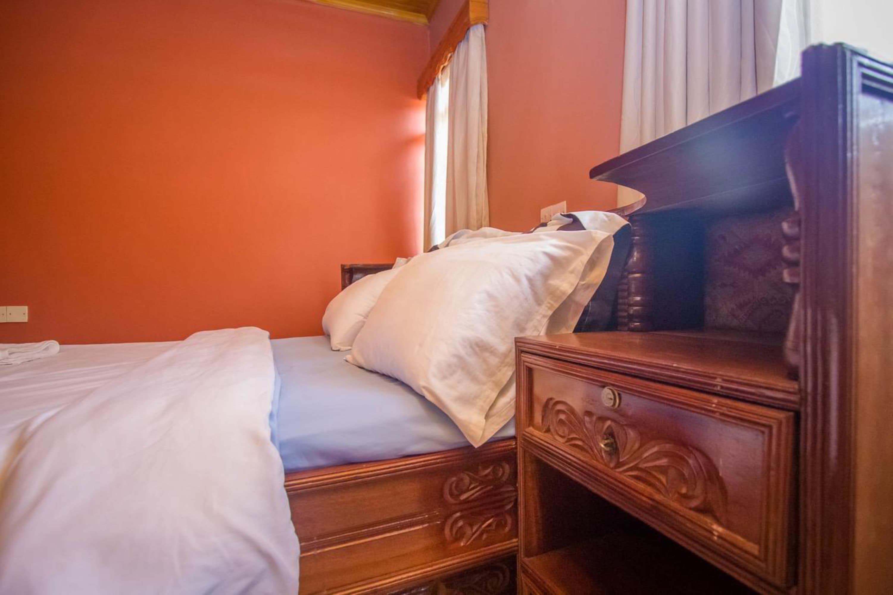 A hotel room with a bed, wooden nightstand, and a window with curtains.