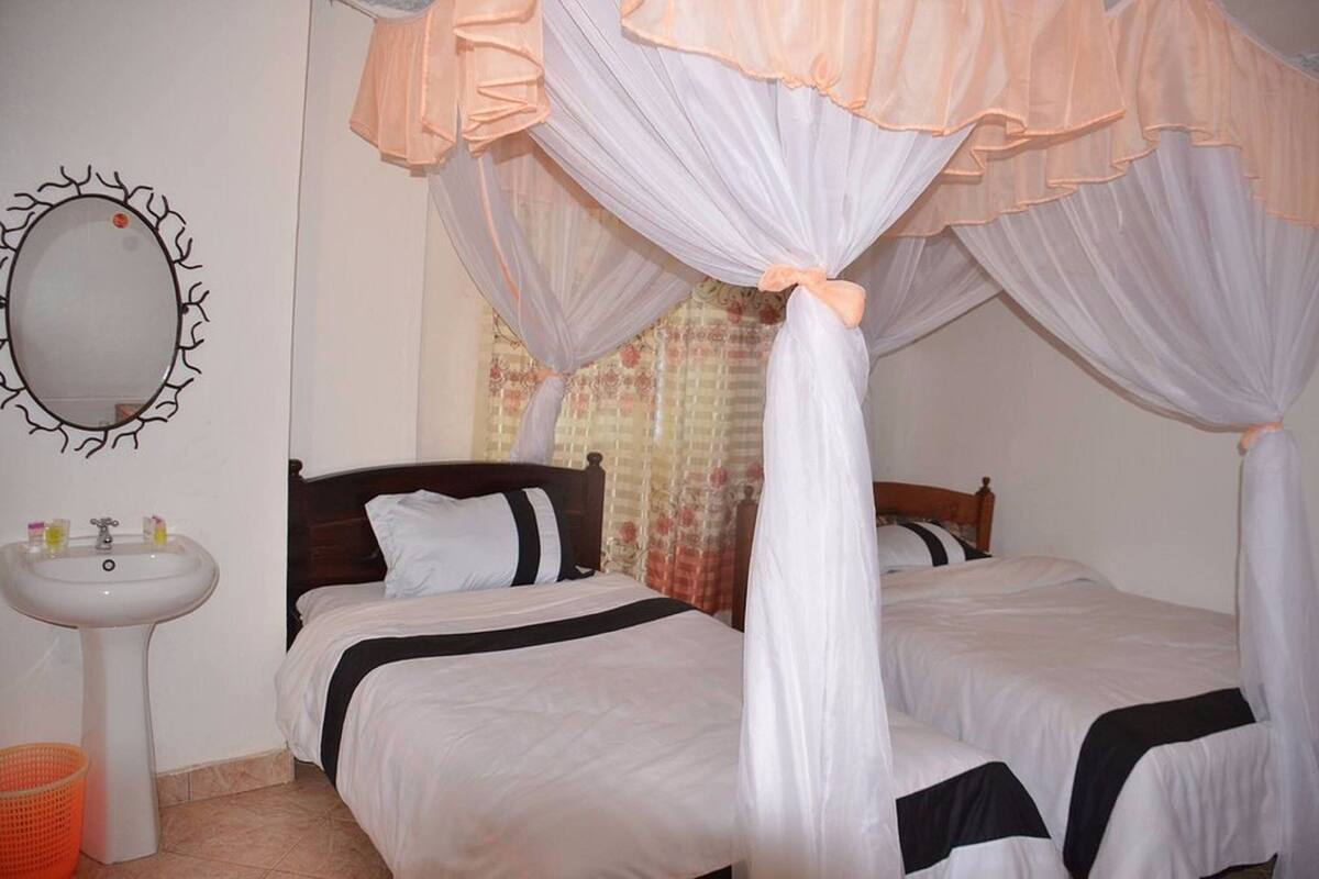 A bedroom with two beds, a bedside table, a mirror, and a sink.