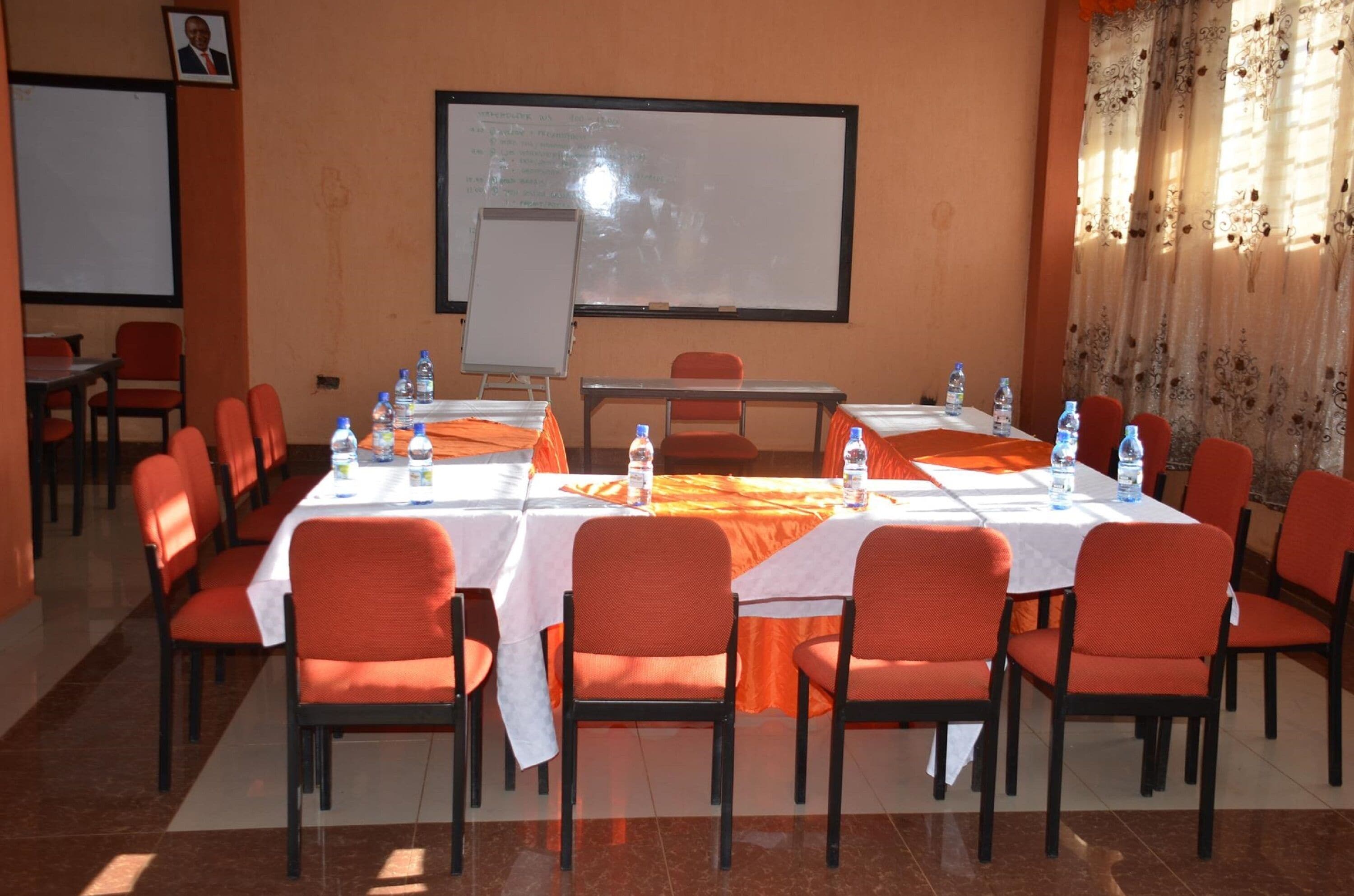 Un salón de conferencias con mesas, sillas, una pizarra y una pantalla de proyector.