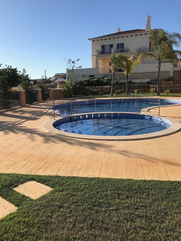 Una piscina con solárium alicatado, rodeada de césped cuidado y palmeras.