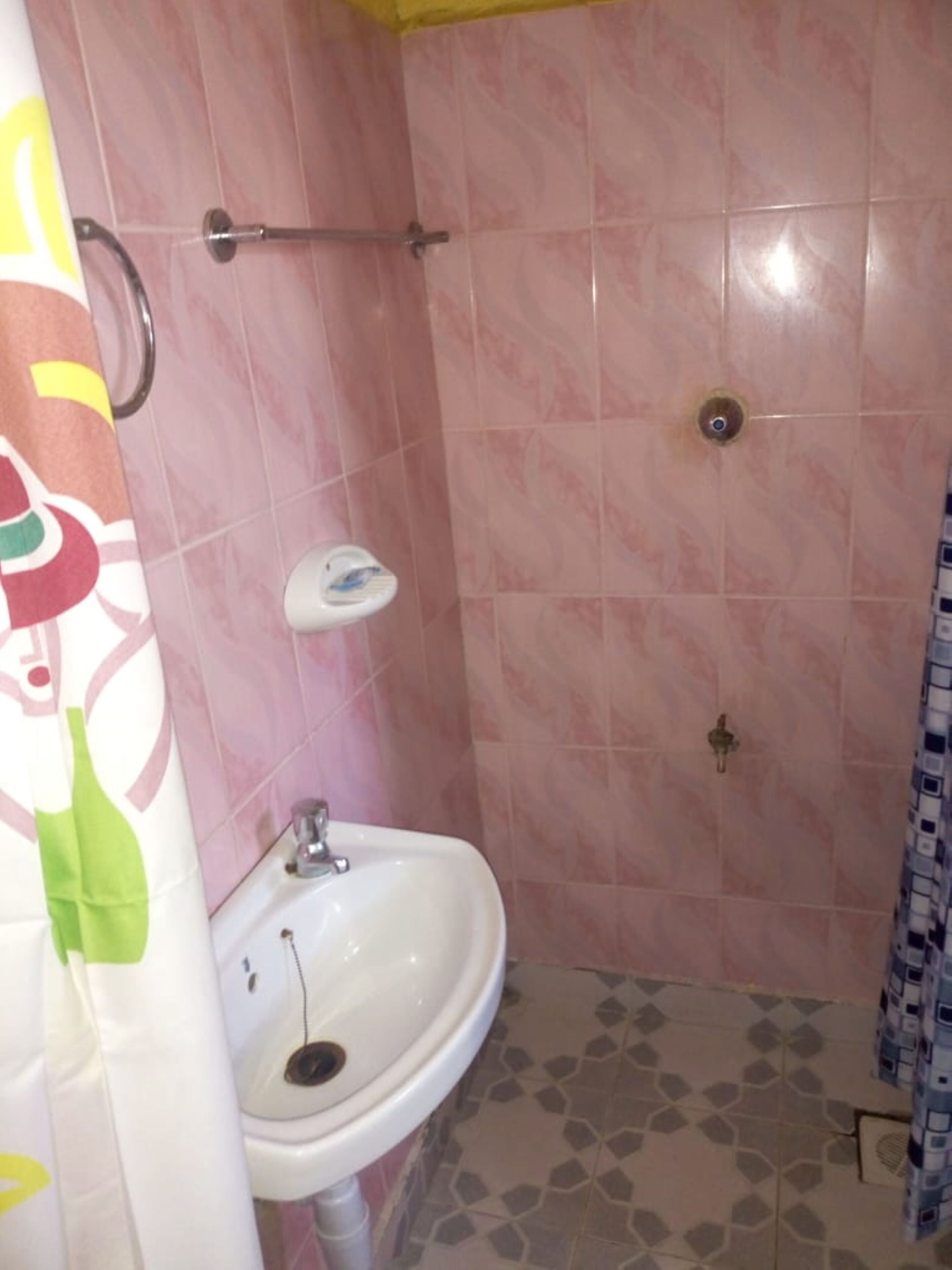 Un baño con azulejos rosa, un lavamanos blanco y una zona de ducha.