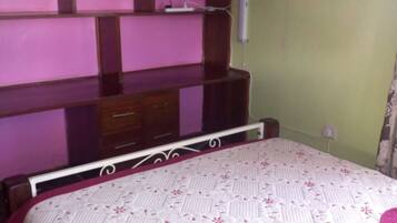 Une chambre à coucher avec un lit, un téléviseur fixé au mur, qui est de couleur rose, et une commode en bois.