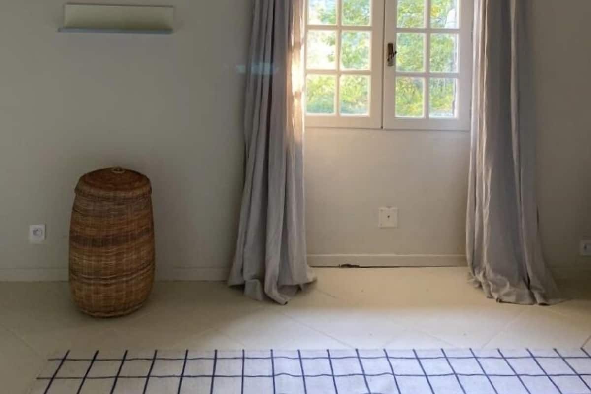A room with a large window, a hanging light fixture, and a woven basket on the floor.