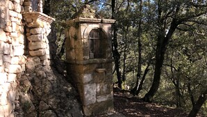 An ancient stone structure with an arched window, surrounded by dense trees and a dirt path. - Ferme le Pavillon (Bargemon)