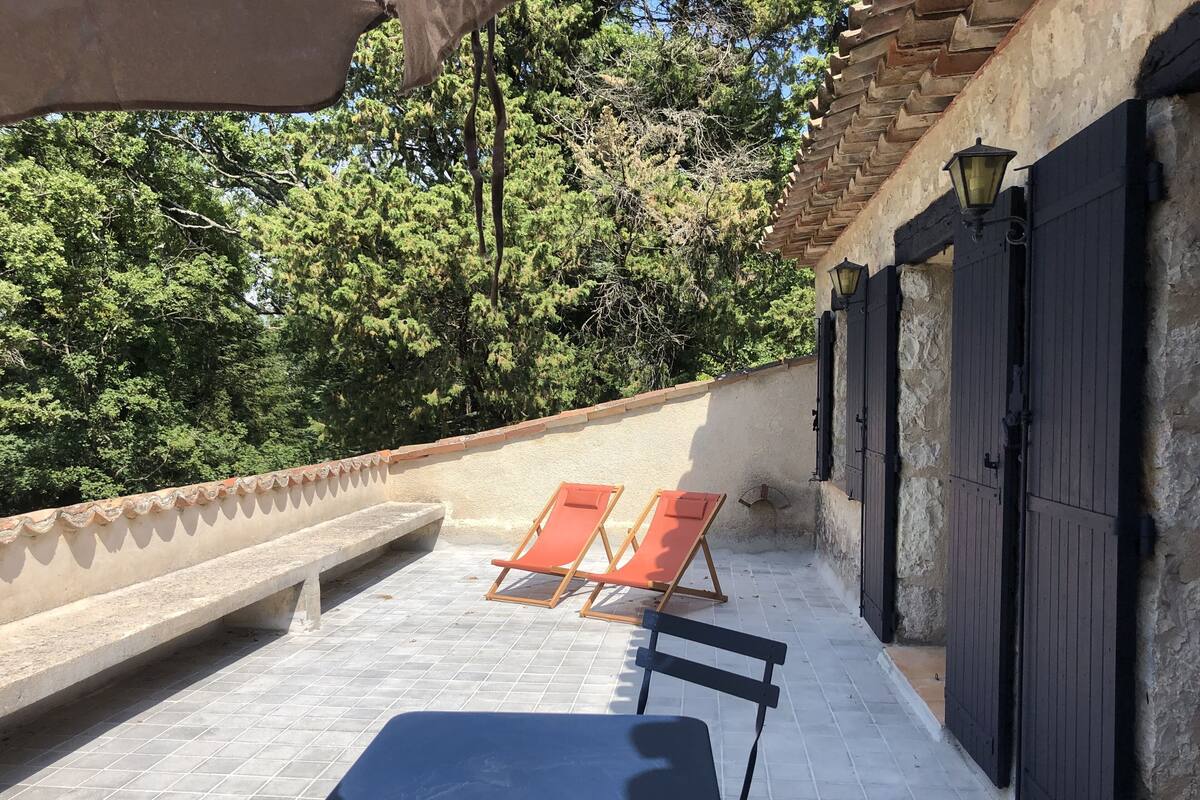 A rooftop terrace with two wooden lounge chairs, a small table, and a stone wall.