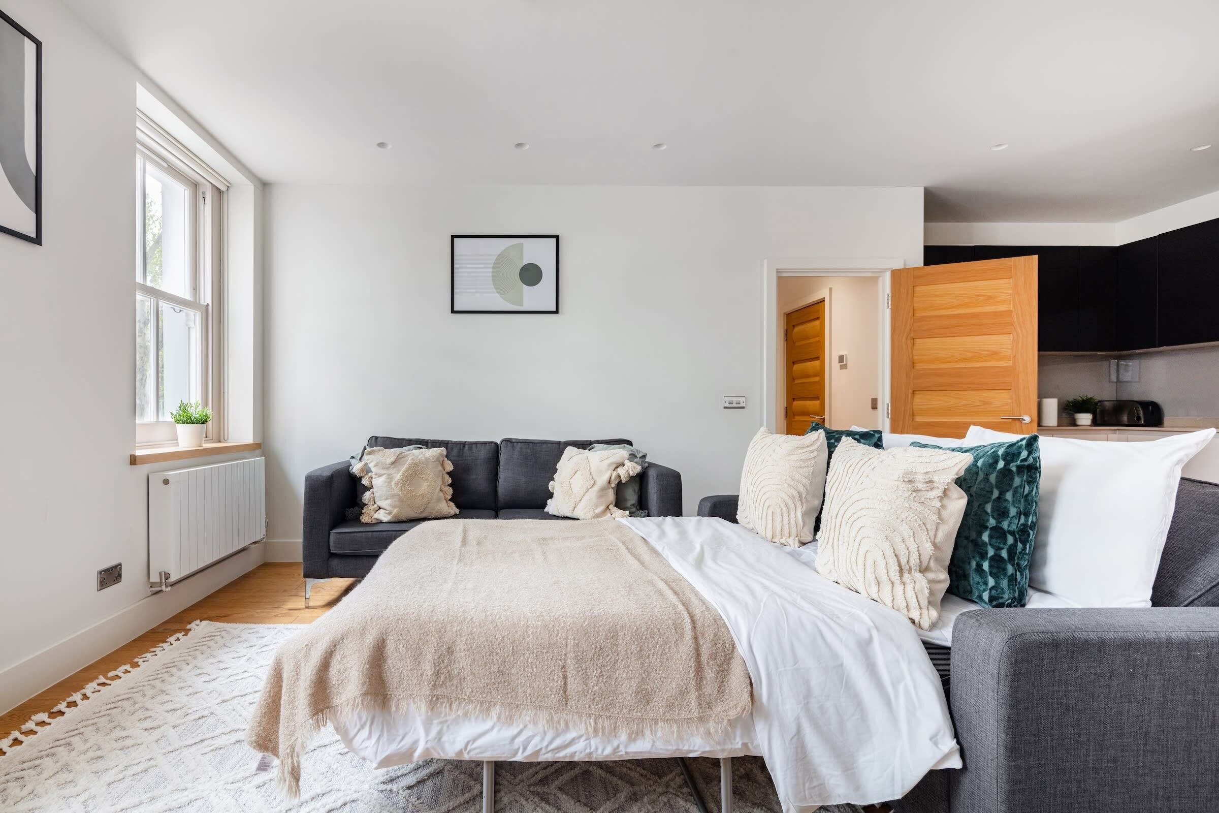 Een moderne slaapkamer met een bed, twee sofa's, een raam en uitzicht op de keuken.
