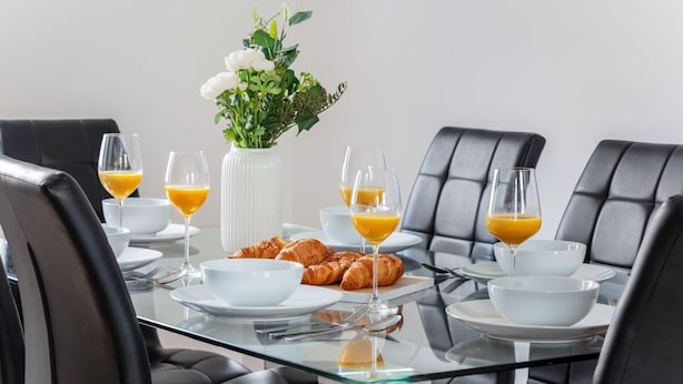 A dining table with breakfast items, including croissants and orange juice, set in a modern room with black leather chairs. - Fitzrovia Spacious 2BR2BA by Bloomsbury (London)