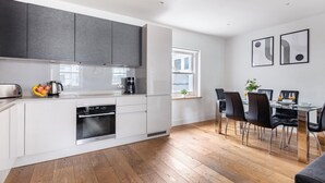 A modern kitchen with white cabinets, a built-in oven, and a dining area with black chairs and a table. - Fitzrovia Spacious 2BR2BA by Bloomsbury (London)