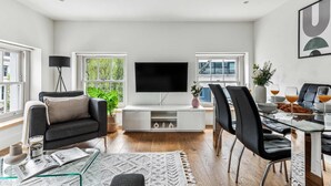 Een moderne woonkamer met een flatscreen televisie, een bank, een eettafel met stoelen en een salontafel met tijdschriften en een kaars.